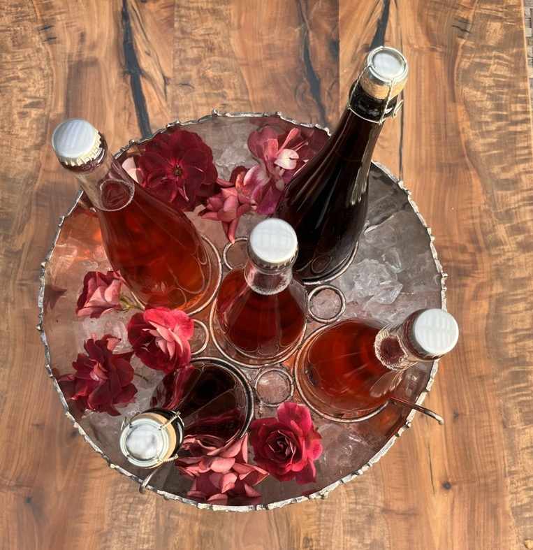 Four bottles of wine in a metal bowl with roses.